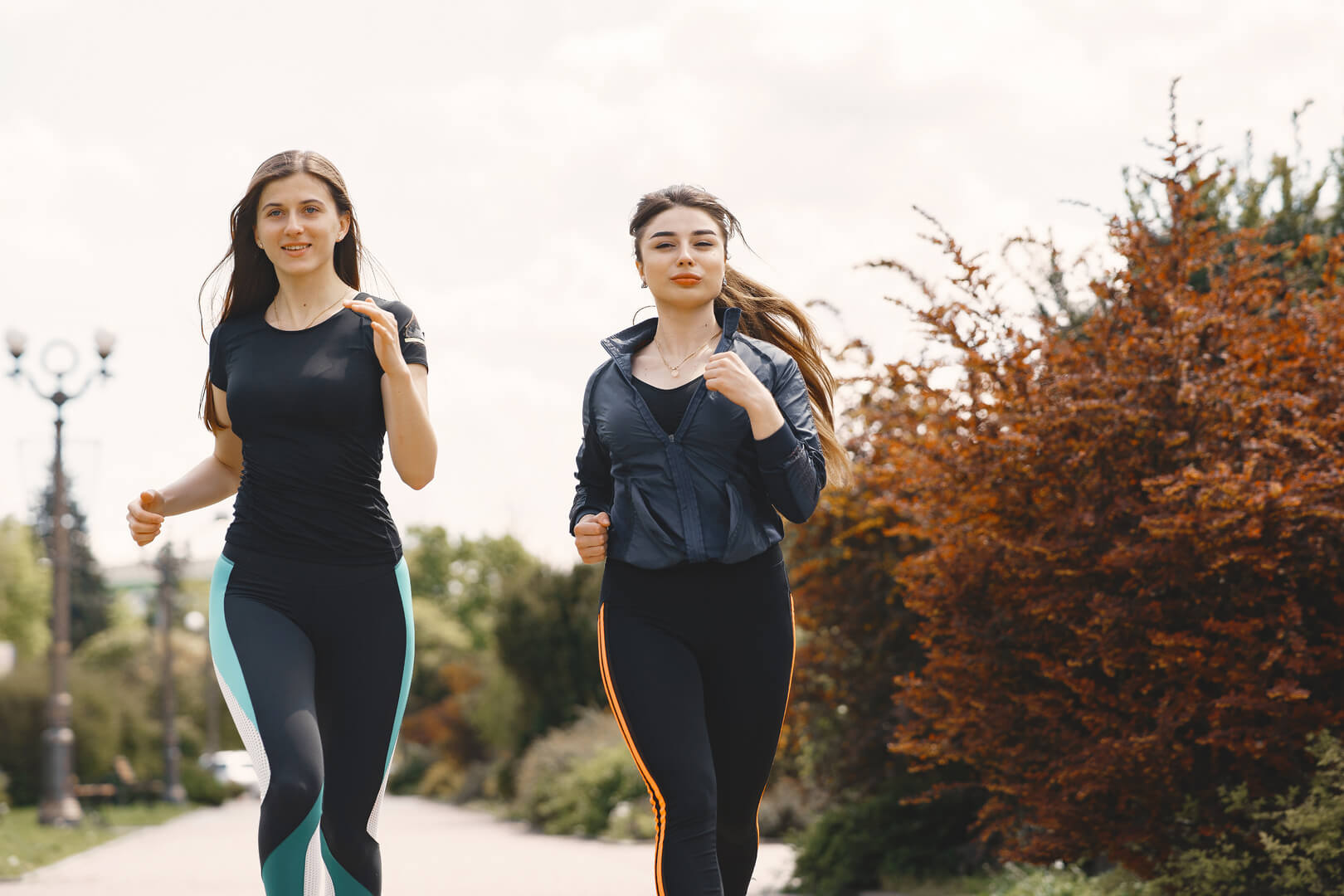 Deux femmes souriantes et dynamiques s'adonnant à une séance de fitness en plein air, illustrant la vitalité, la complicité et le bien-être dans la pratique sportive.